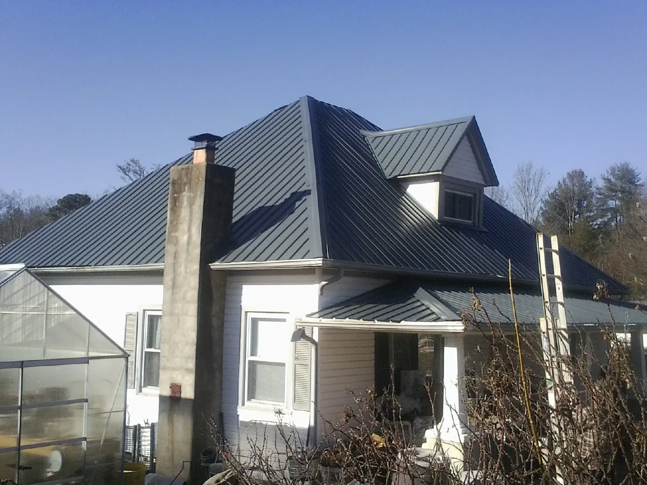 Dark blue standing seam metal roof on a white farmhouse with dormer — Slate & Tile Roof Repair by Roofing Brothers in Lime Ridge