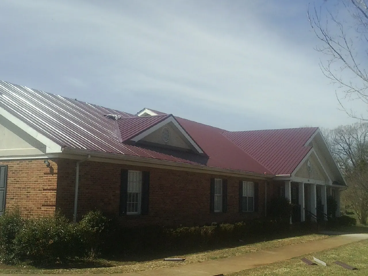 Red metal roof with gabled entries on a long brick building, from a Hail Damage Roof Repair job in Lime Ridge