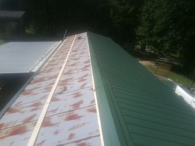 Old rusted panels beside newly installed green metal roofing in Lime Ridge