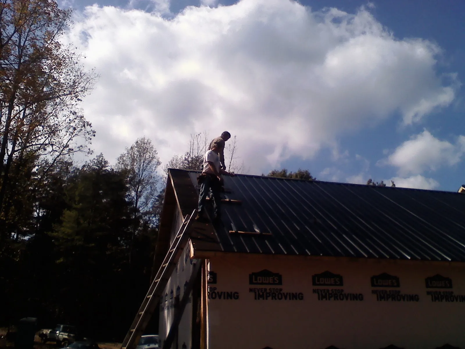 Roofer fastening dark metal panels high against a cloudy sky, from a Roof Inspection job in Lime Ridge