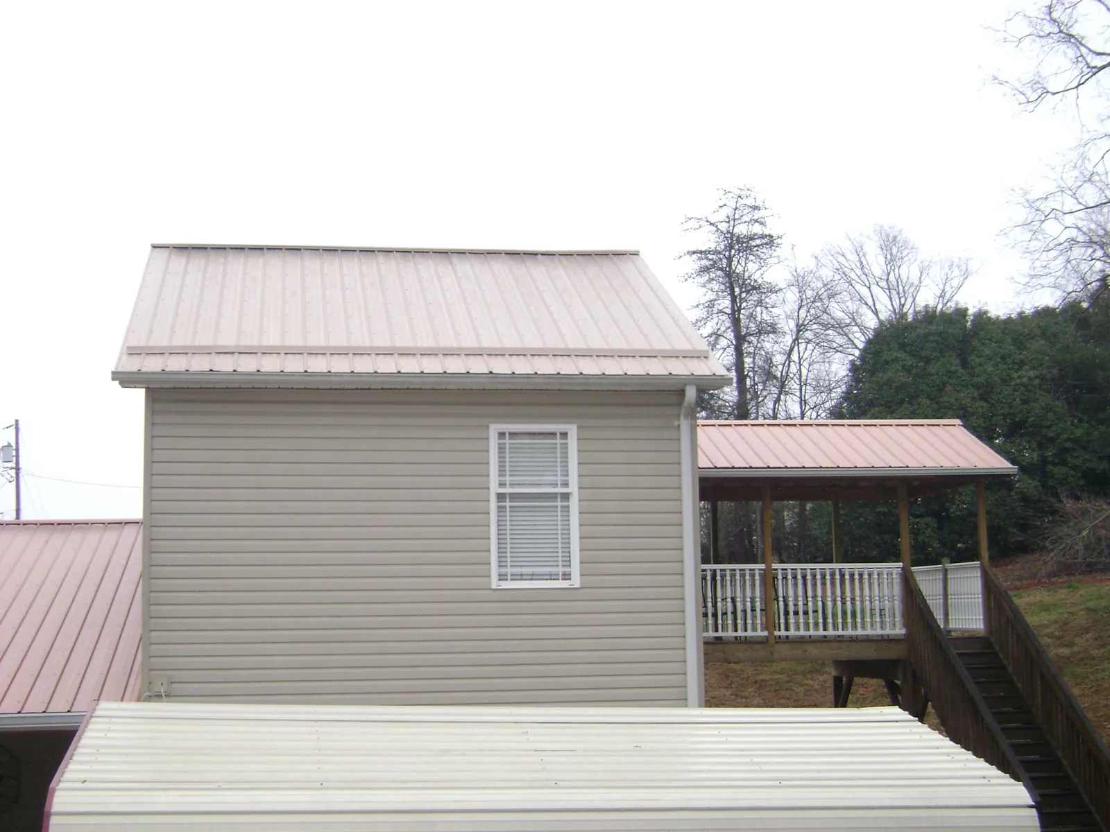 Tan metal roofs on a two story addition and attached porch, from a Roof Replacement job in Lime Ridge